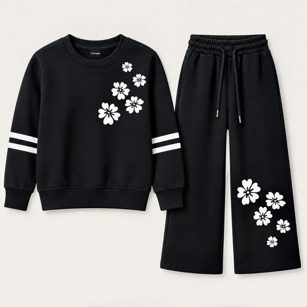 Girl's black two-piece sweatsuit featuring a crewneck sweatshirt with white floral print and matching wide-leg sweatpants with drawstring waist and floral details.